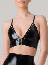 A model wearing a black latex bra with gold front zip and studs, paired with matching black latex knickers.