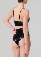 Back view of a model wearing a black latex lingerie set with longline triangle bra and high waisted knickers, featuring adjustable shoulder straps, gold front zip and stud detailing at bust.