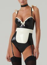 A model wearing a black and white latex costume with frilled shoulders, a mini bow at the front, adjustable straps, an apron, a choker, and a hair bow. Worn here with black stockings.