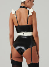 Back view of a model wearing a black and white latex costume with frilled shoulders, a mini bow at the front, adjustable straps, an apron, a choker, and a hair bow. Worn here with black stockings.