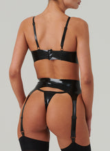 Back view of a model wearing a black latex rubber lingerie set, including bra, suspender belt and g-string. Black stockings also worn.