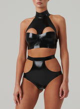 A model wears a black latex bra top by William Wilde with a high collar and keyhole cut-outs, worn with black latex knickers with hip cut-outs, against a neutral background.
