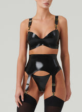 A black shiny latex lingerie set worn by a model. The set includes a bra and suspender belt, both with gold metal sliders, press studs and suspender clips. Worn with matching G-String and black opaque stockings. All by designer William Wilde