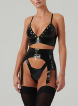 A model wearing a black latex lingerie set and black stockings. The set includes gold studded bra and suspender belt, both with gold front zips, and matching latex thong.