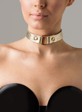 A gold leather choker with a central O-ring, displayed on a person wearing a black latex strapless top.