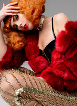 A model with bright orange hair wears a gold leather choker, red fur coat, black latex bra and trousers made of gold leather and chain.