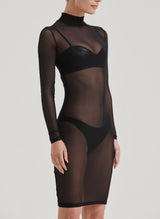 A model wearing a black mesh pencil dress with long sleeves, a high neck, and a keyhole at back, paired with black latex lingerie, visible underneath.