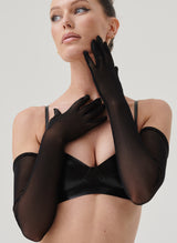 A model wearing long black semi-sheer mesh gloves, paired with a black latex bra, on a grey background.
