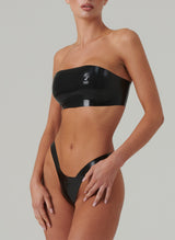 A model wearing a black latex bandeau bra and matching high leg thong.