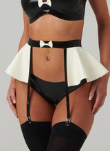A close up of a model wearing a black and white latex suspender belt with four garter straps. The belt has a flared peplum and mini bow at front. Worn here with matching briefs and stockings.