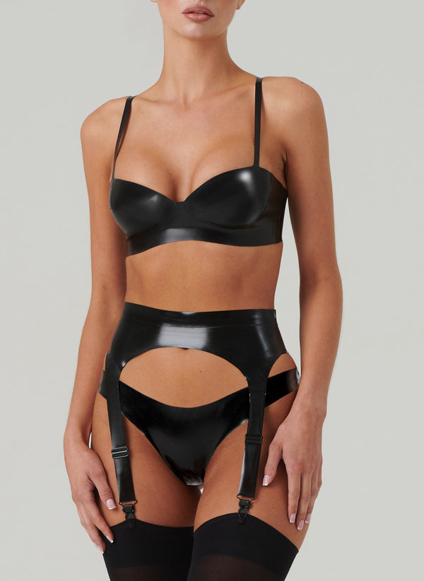 Person wearing a black latex rubber lingerie set on a plain background